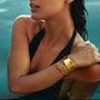 Woman wearing a gold iris petal cuff, showcasing its intricate design while in water.