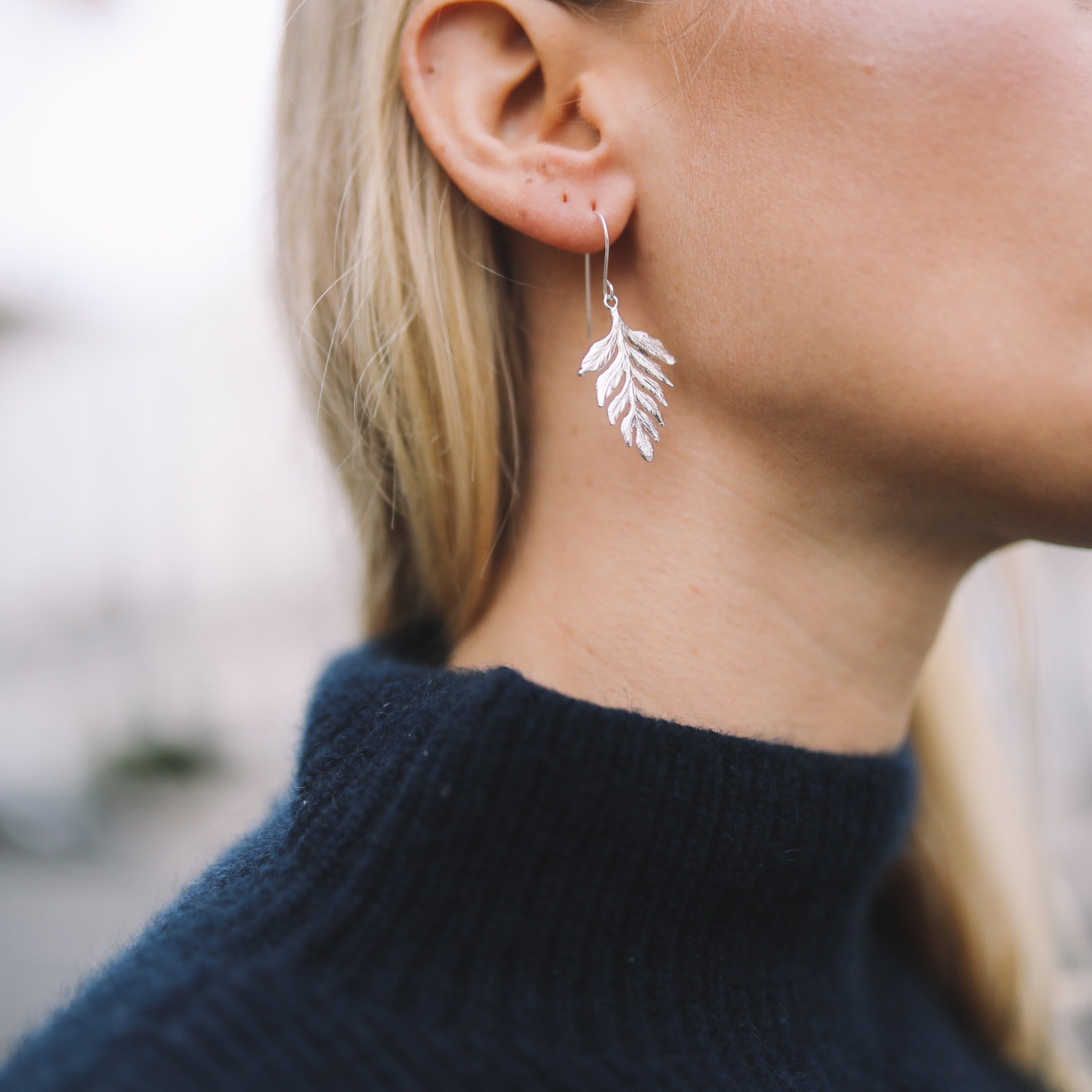 Silver fern charms on drop earrings worn on womans ear