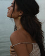 Gold fern drop earrings worn by model by the water, showcasing their elegant design and perfect for any occasion.