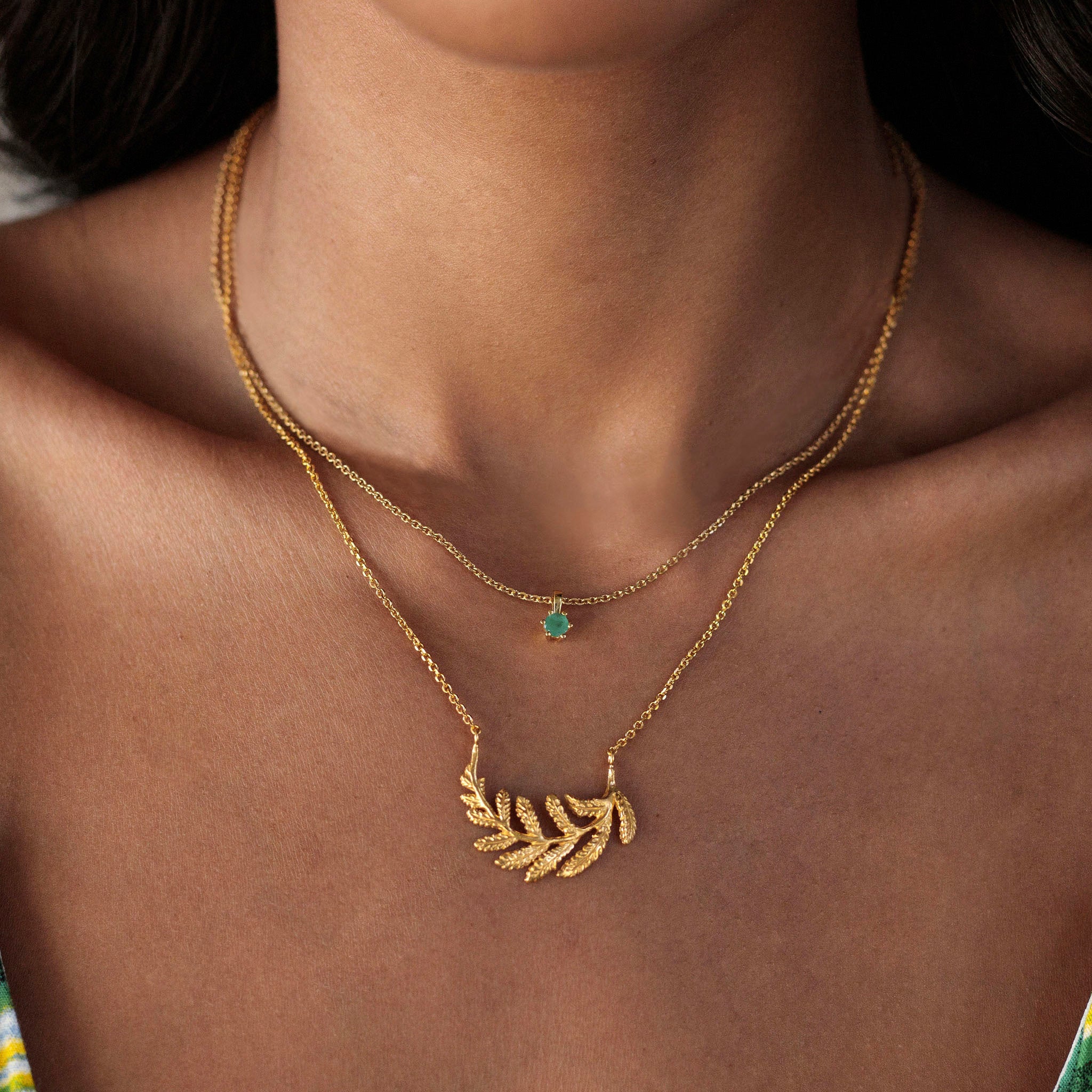 Emerald and fern necklace set featuring a fern-inspired hoop necklace and emerald pendant on a model.