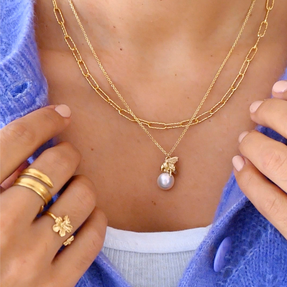 Gold Honeybee and Moonlight Pearl Pendant showcased on a layered gold necklace with a blue cardigan.
