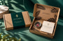 Zoraida Heirloom Fingerprint Pendant Pack shown in its packaging, featuring a closed box with a dark green band and an open box displaying a small tin of pink beads and a card inside a brown kraft box with leaf patterns.