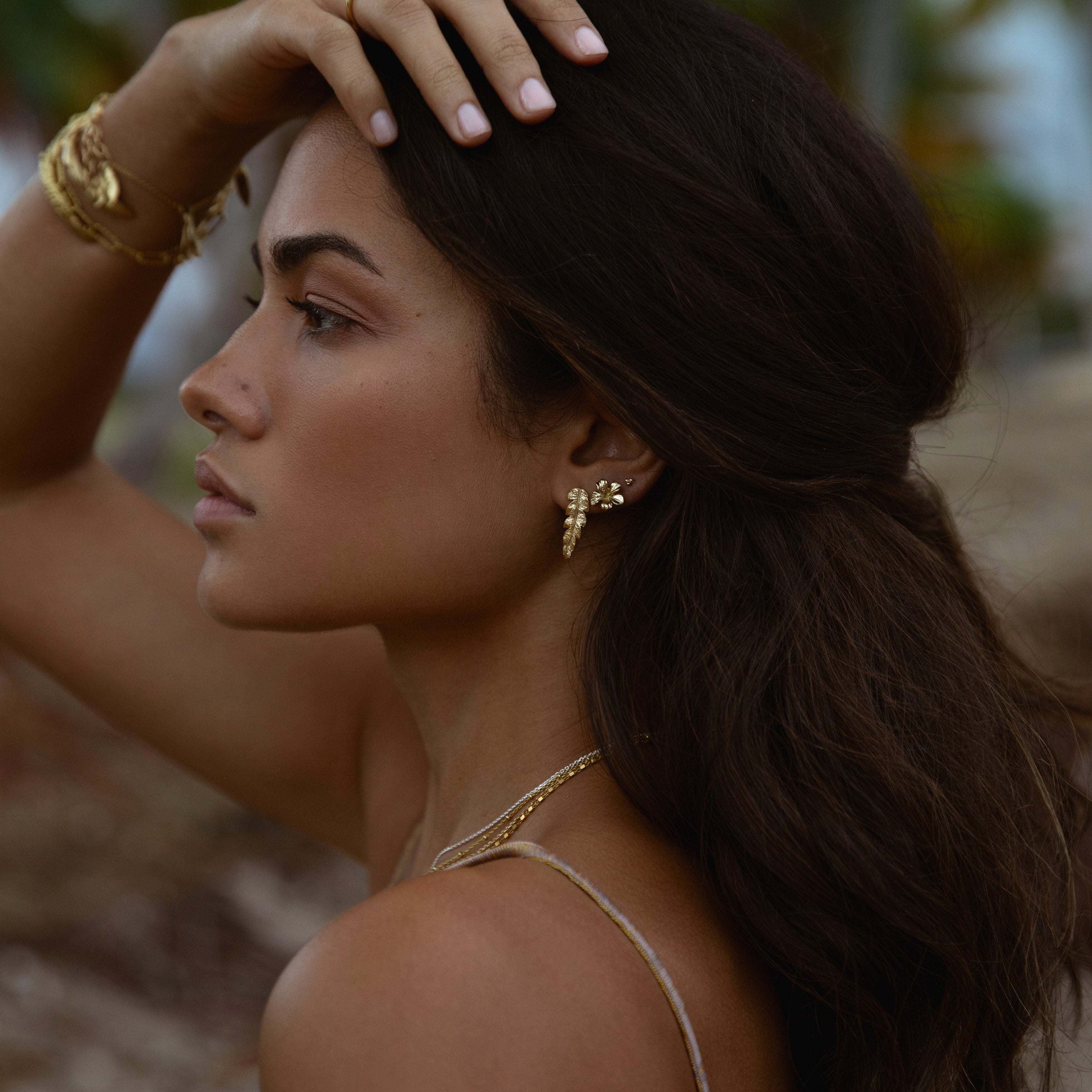 Gold hibiscus sweet nectar stud earrings worn by a model showcasing elegant jewelry in a natural setting.
