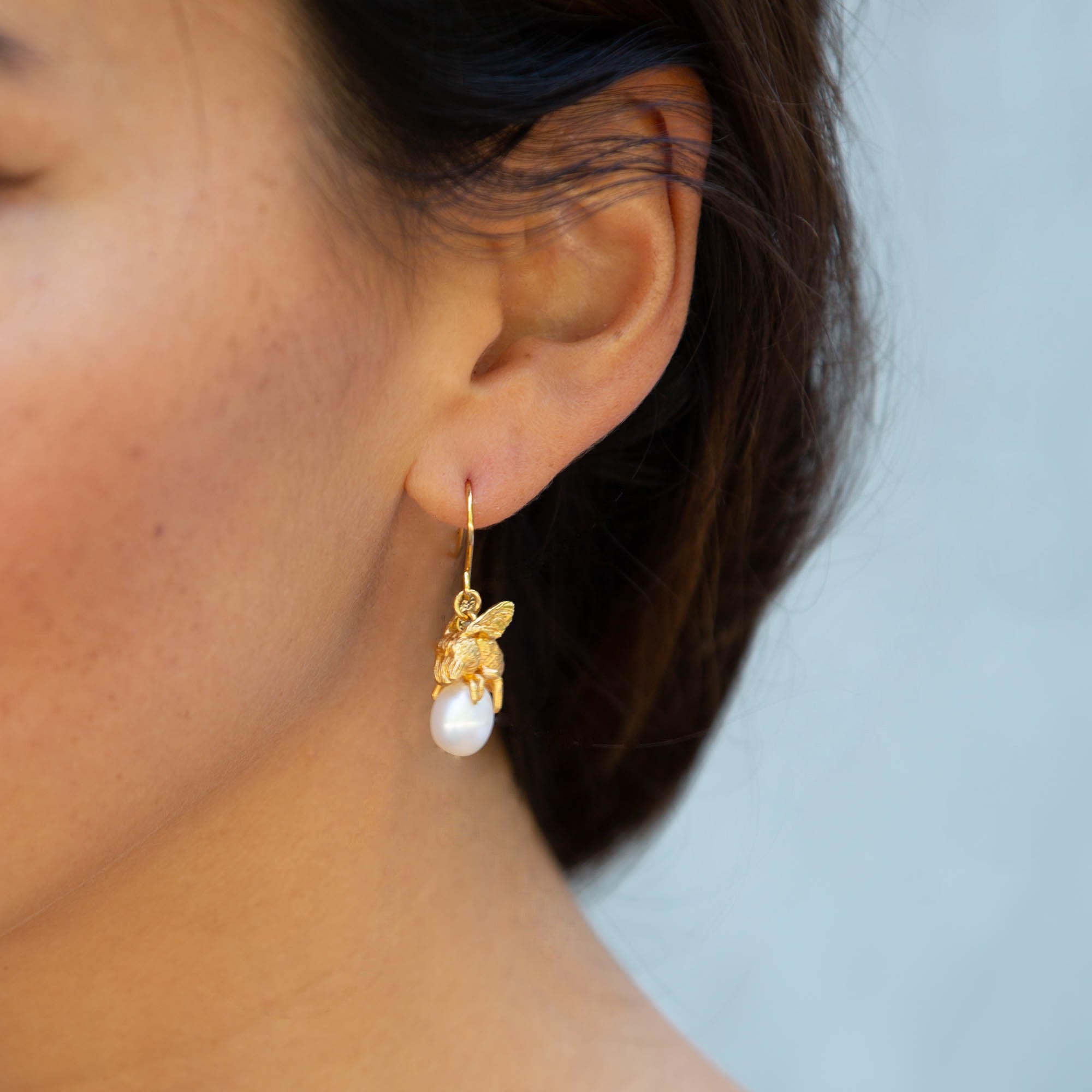  Silver honeybee resting on a pearl charm on earrings worn on womans ear