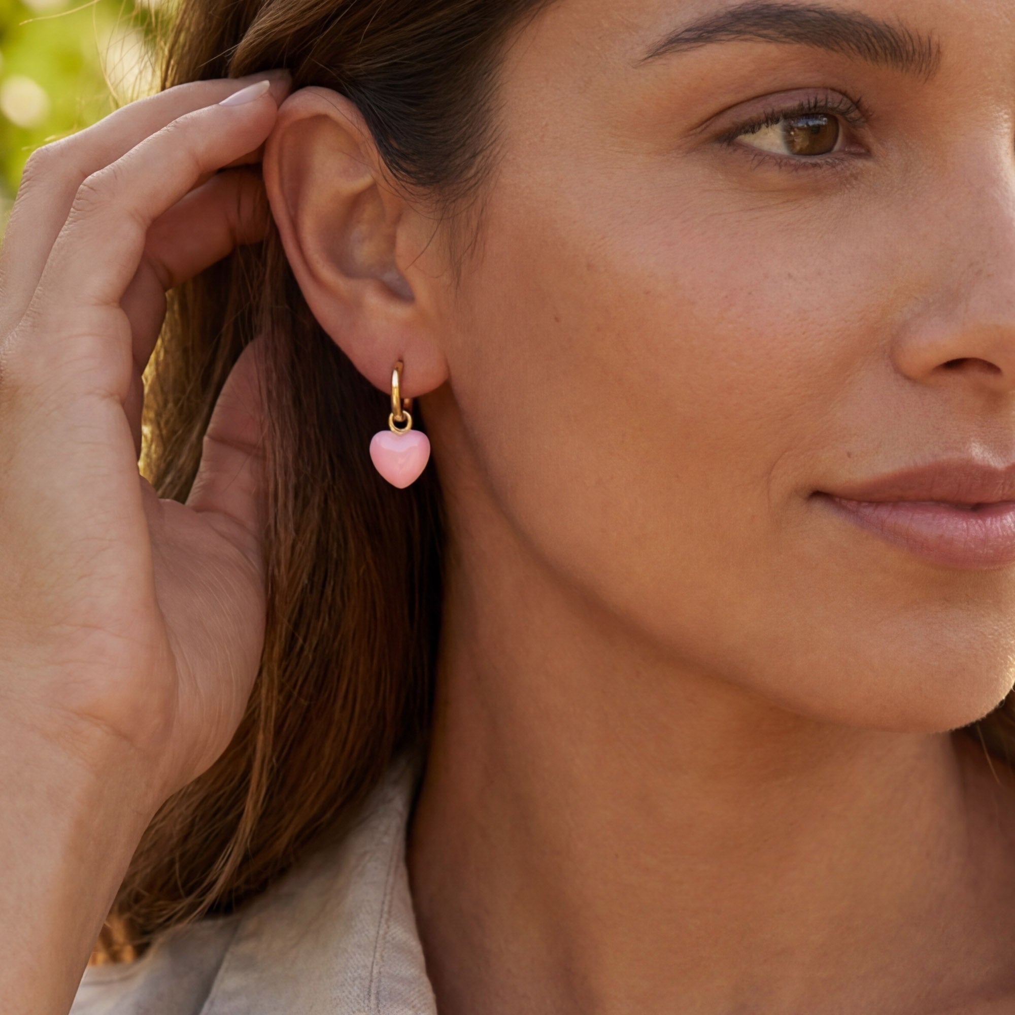 A model wearing Pink Shell Love Heart Hoop Earrings, featuring a pink heart charm and gold hoop.