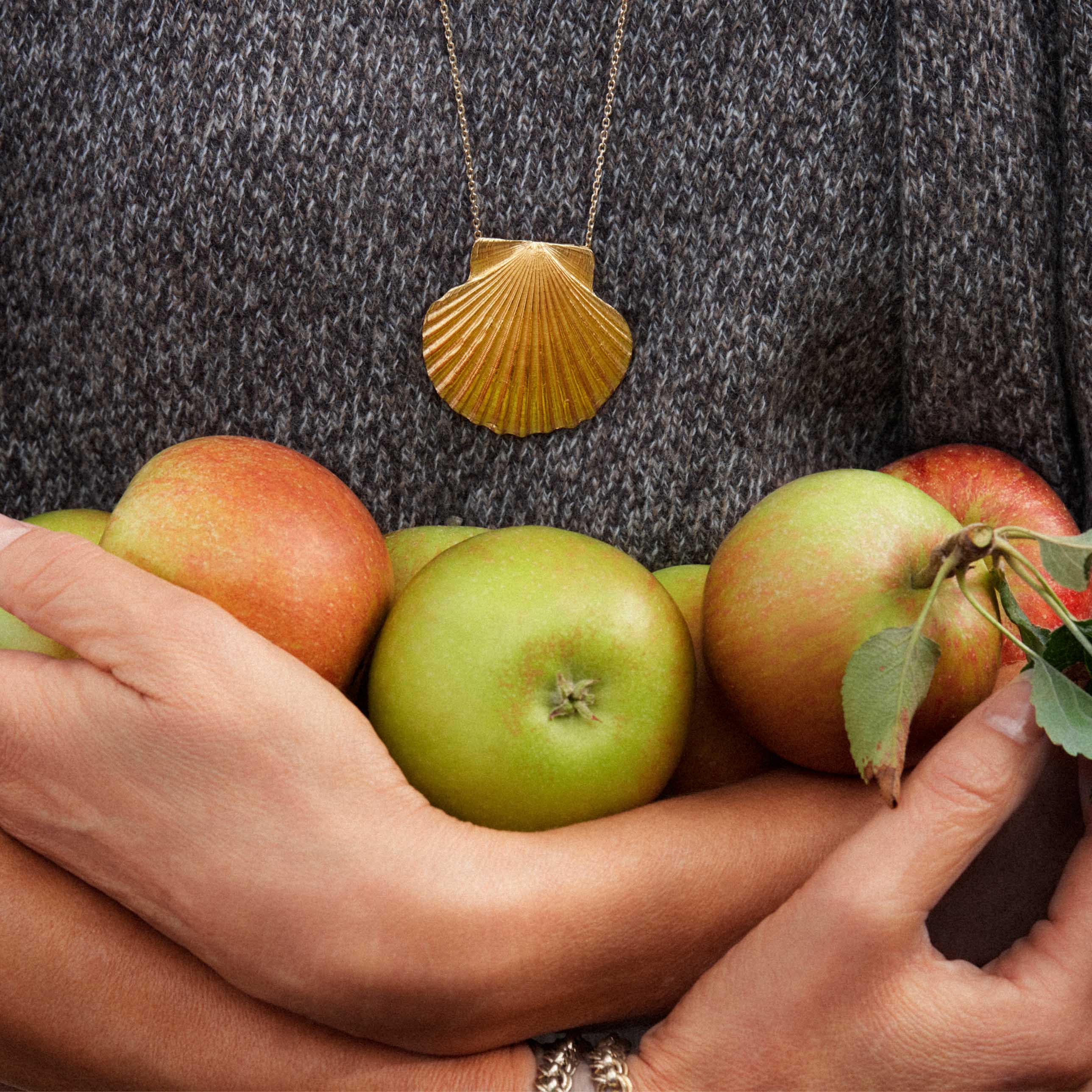 Gold Scallop Shell Pendant worn by a person holding fresh apples, showcasing coastal elegance and style.