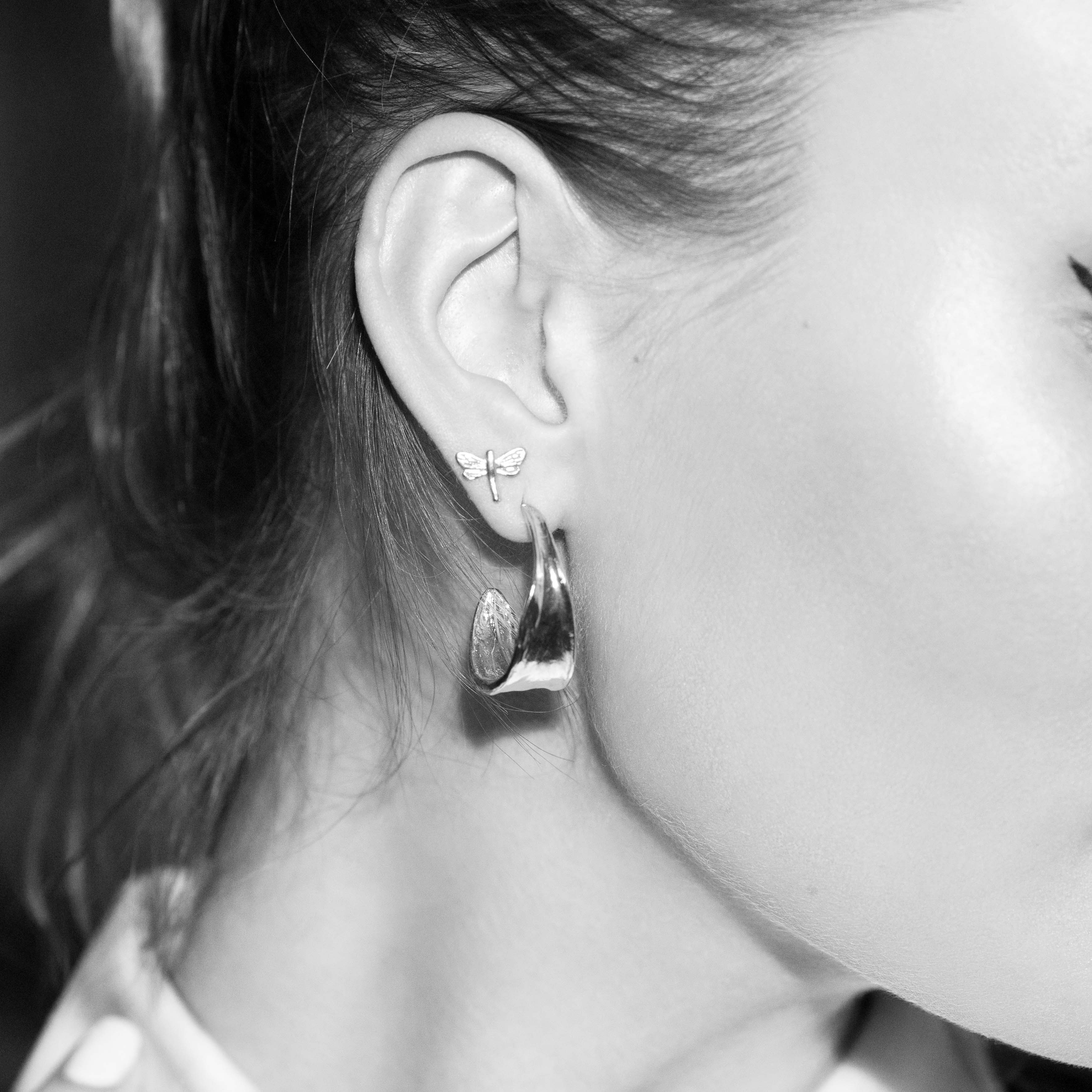 Close-up of a model wearing silver iris petal hoop earrings and delicate butterfly stud earrings.
