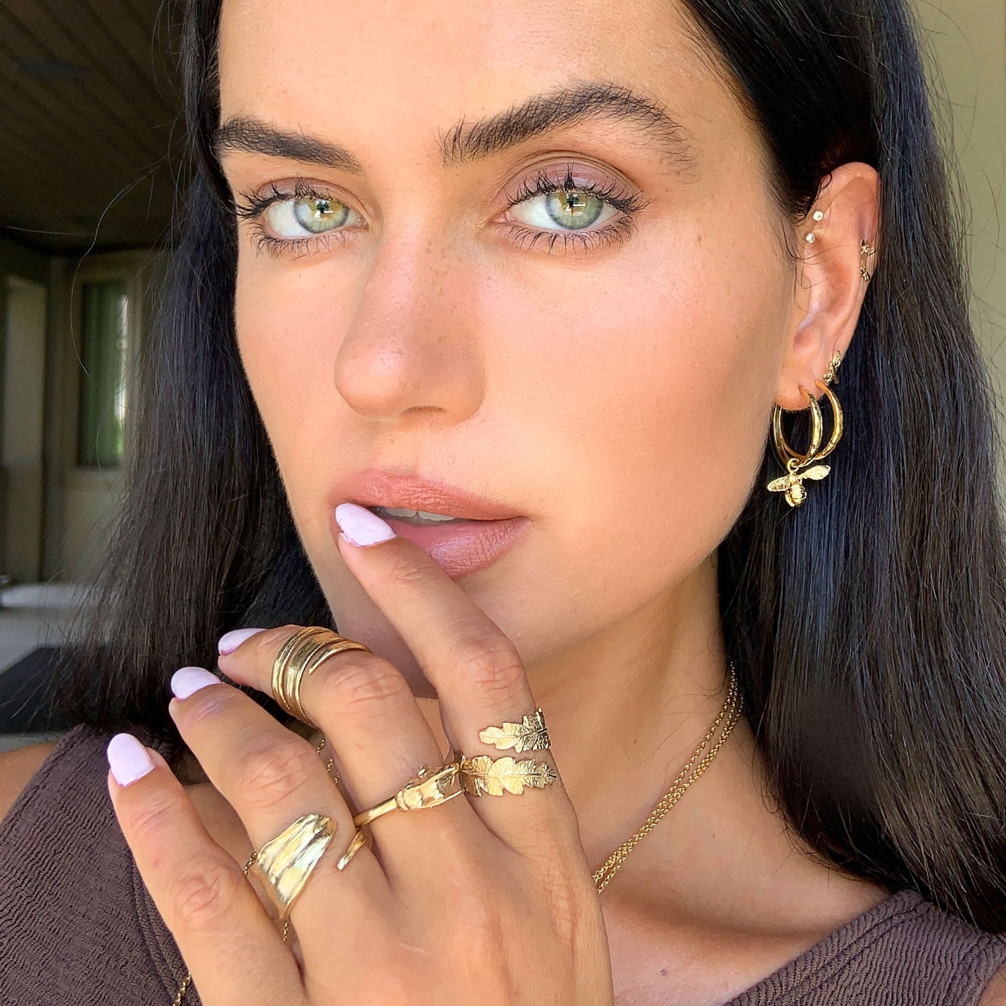 Close-up of a model wearing Gold Little Bee Hammered Hoop Earrings and multiple gold rings.