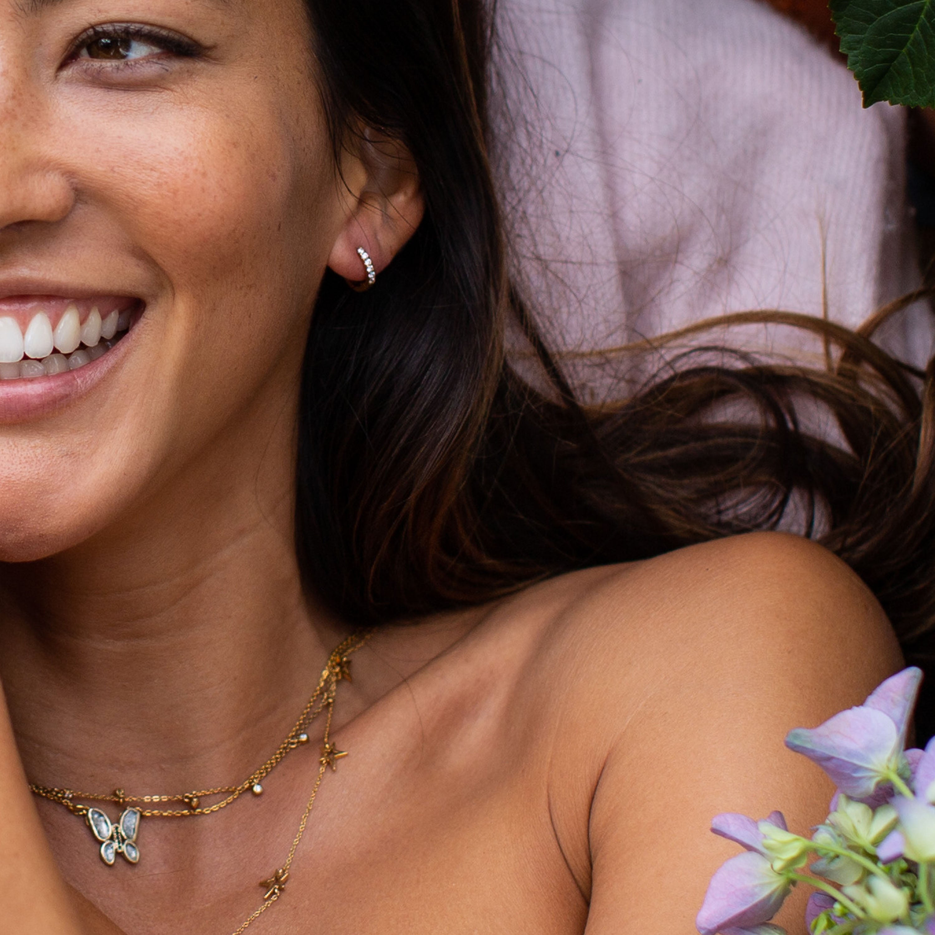 Gold Glitter Huggie Hoop Earrings worn by a smiling woman with long hair and layered necklaces.