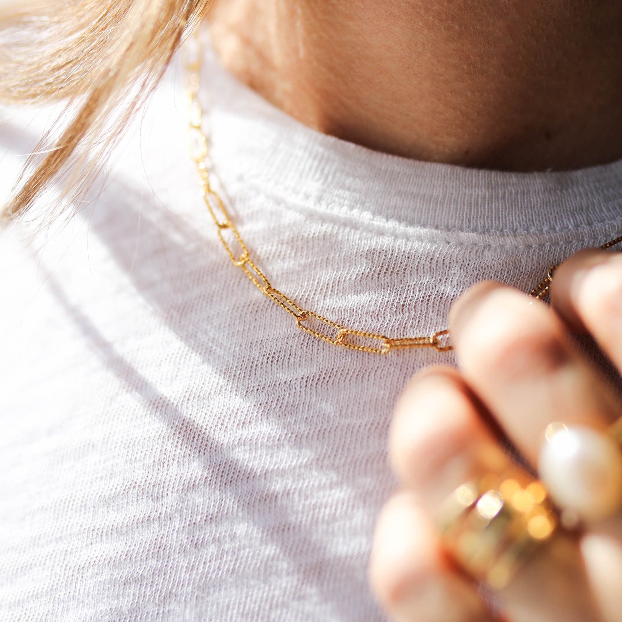 Close-up of a person wearing a silver glitter chain necklace with shimmering details against a white shirt.
